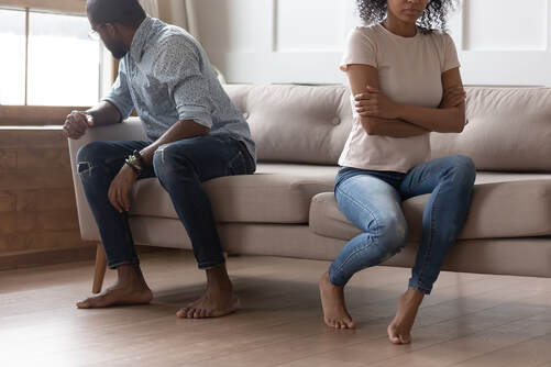 Couple arguing after learning one of them cheated. They are sitting on a sofa with backs to each other, looking angry, upset and hurt by infidelity. You can get therapy for infidelity in Plymouth, MN to recover from an affair with affair recovery online counseling in Minnesota.