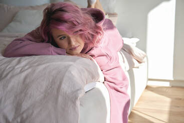 Woman laying on a bed with pink hair and a pink sweatshirt, feeling concerned about PTSD and needing EMDR therapy for sexual trauma therapy in Minneapolis, MN and beyond with online therapy in Minnesota