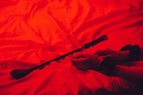 Flogger on a red background  with hands reaching toward it. You can learn more about kink and BDSM from an expert sex therapist in Plymouth, MN here. Read the sex therapy blog or start sex therapy near Minneapolis, MN here. 55311 | 55305 | 55343