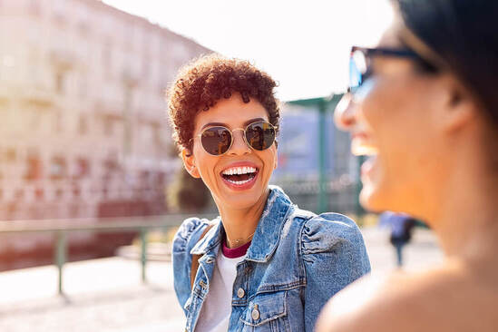 Queer woman laughing and smiling with another woman in the Twin Cities. You can feel confident in your queerness with an LGBTQ+ affirming therapist in Plymouth, MN. 55311 | 55305 | 55343