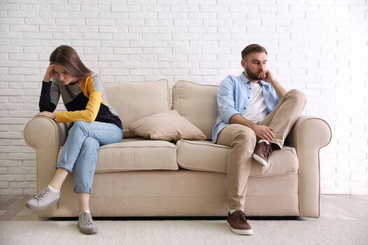 Unhappy couple sitting on two different ends of a couch looking upset after a fight about their sexual values. You can get help with sex therapy in Minnesota and counseling in Plymouth, MN for couples therapy, marriage counseling and sexual preferences. Get online therapy in Minnesota here too! 