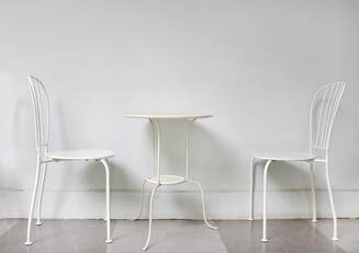Photo of two, simple white chairs, facing each other across a white table against a white/light gray background. Couples counseling, sex therapy in the Minneapolis area