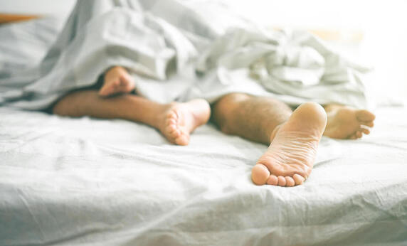 Couples' feet in bed under the covers. Sex addiction and problematic sexual behavior can be addressed in sex therapy. Meet with a sex therapist in Plymouth, MN to discuss sexual performance anxiety here. 55447 | 55441 | 55442