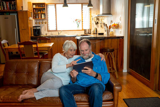 Older couple sitting on couch looking at a iPad and snuggling. You can get help from a skilled sex therapist in Plymouth, MN with online therapy in Minnesota for couples therapy and marriage counseling for sexual concerns and mismatched desire. 55446