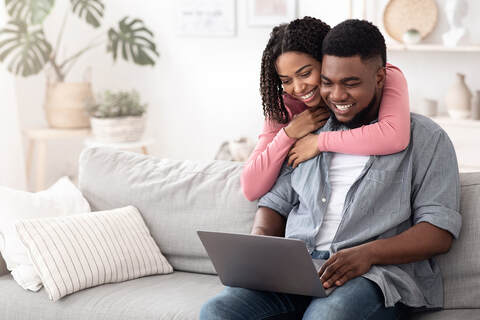Couple embracing and looking at a computer together at home on the couch looking for more connection with Gottman couples therapy and marriage counseling with sex therapists from Sexual Wellness Institute in Plymouth, MN. 