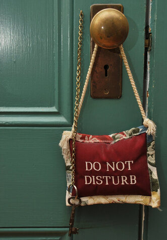 Picture of a green door with a pillow hanging off of the doorknob that says 