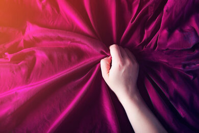 Picture of a woman's hand holding tightly to pink silk sheets, presumably during an orgasm. Are you looking for 