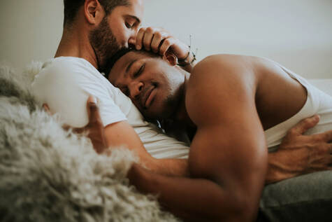 Couple holding each other on the bed, snuggling and looking comfortable together. As a gay couple, they want to find connection with an LGBTQ affirming therapist in Minnesota. They are sharing a sweet moment as he kisses her forehead. They went to marriage counseling or couples therapy with a Gottman trained therapist or EFT treatment specialist to talk about low desire, low libido, mismatched desire and other sexual concerns in Plymouth, MN 55446. 