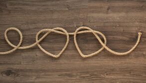 One piece of burlap string forming two hearts on a wood grain background. Two hearts, bonded together, exploring connection in Minnesota sex therapy.